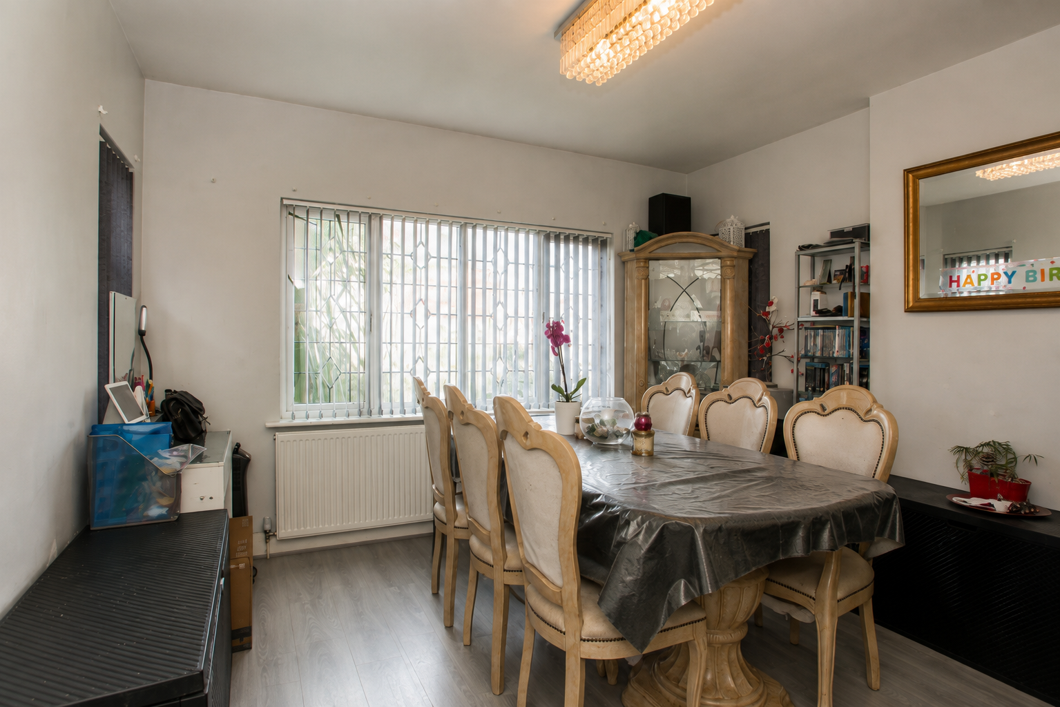 A dining room with a table seating eight, wood-effect flooring and a front-facing window